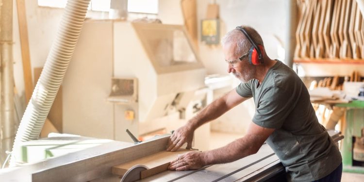 Piła stołowa tnie deskę w garażu podczas remontu domu z narzędziami w tle