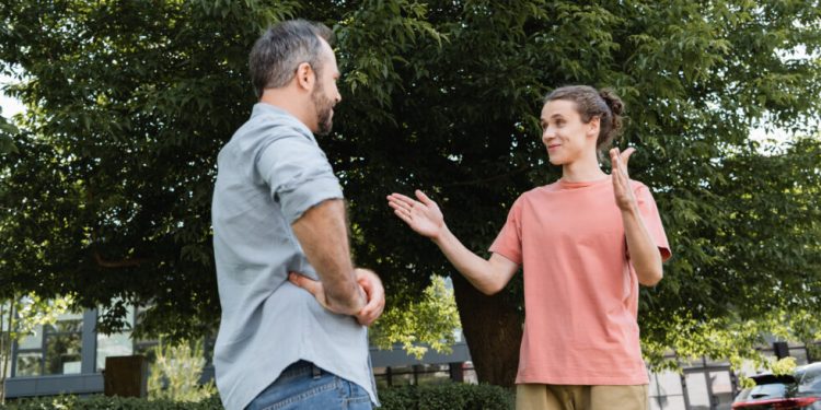 happy teenage boy showing big gesture with hands near bearded father in park