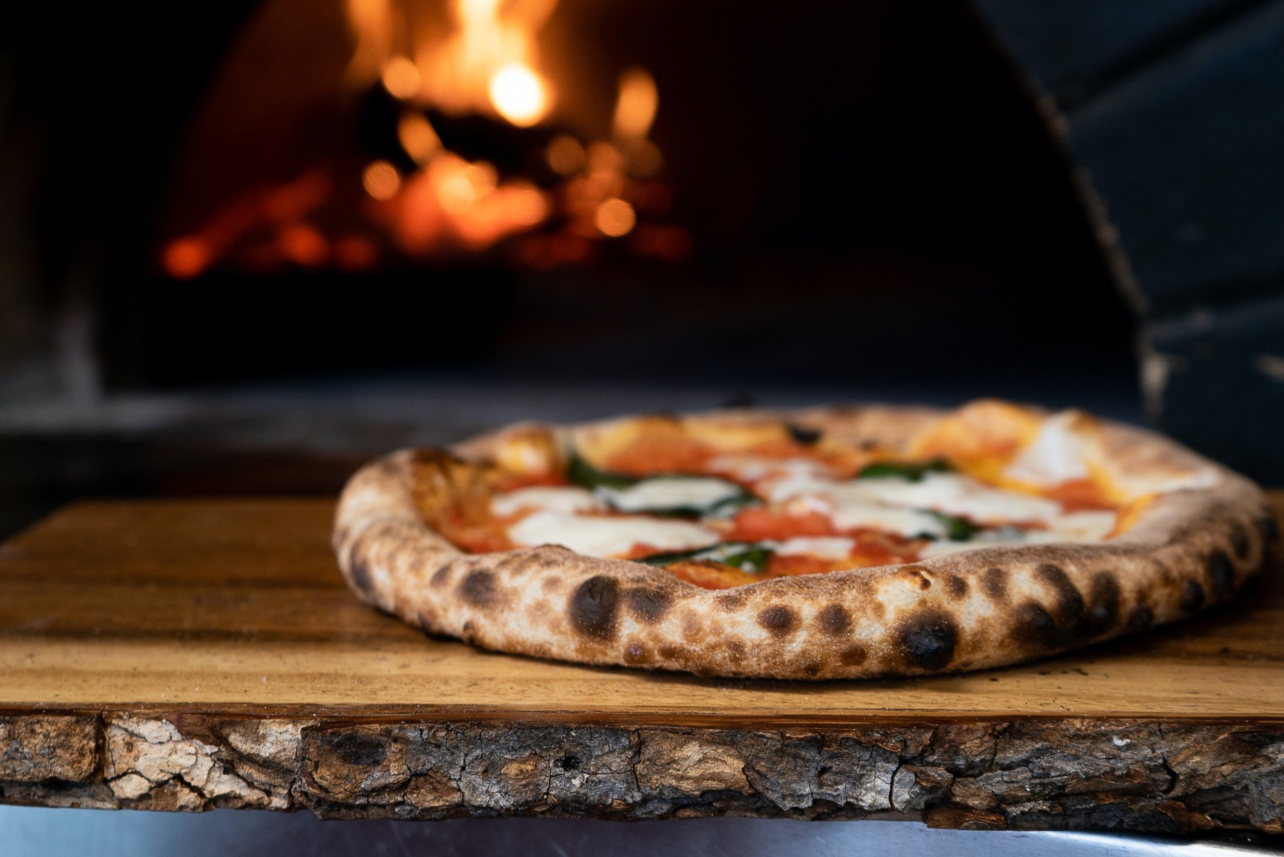 gruba, soczysta pizza w drewnianym piecu z widocznym spodem