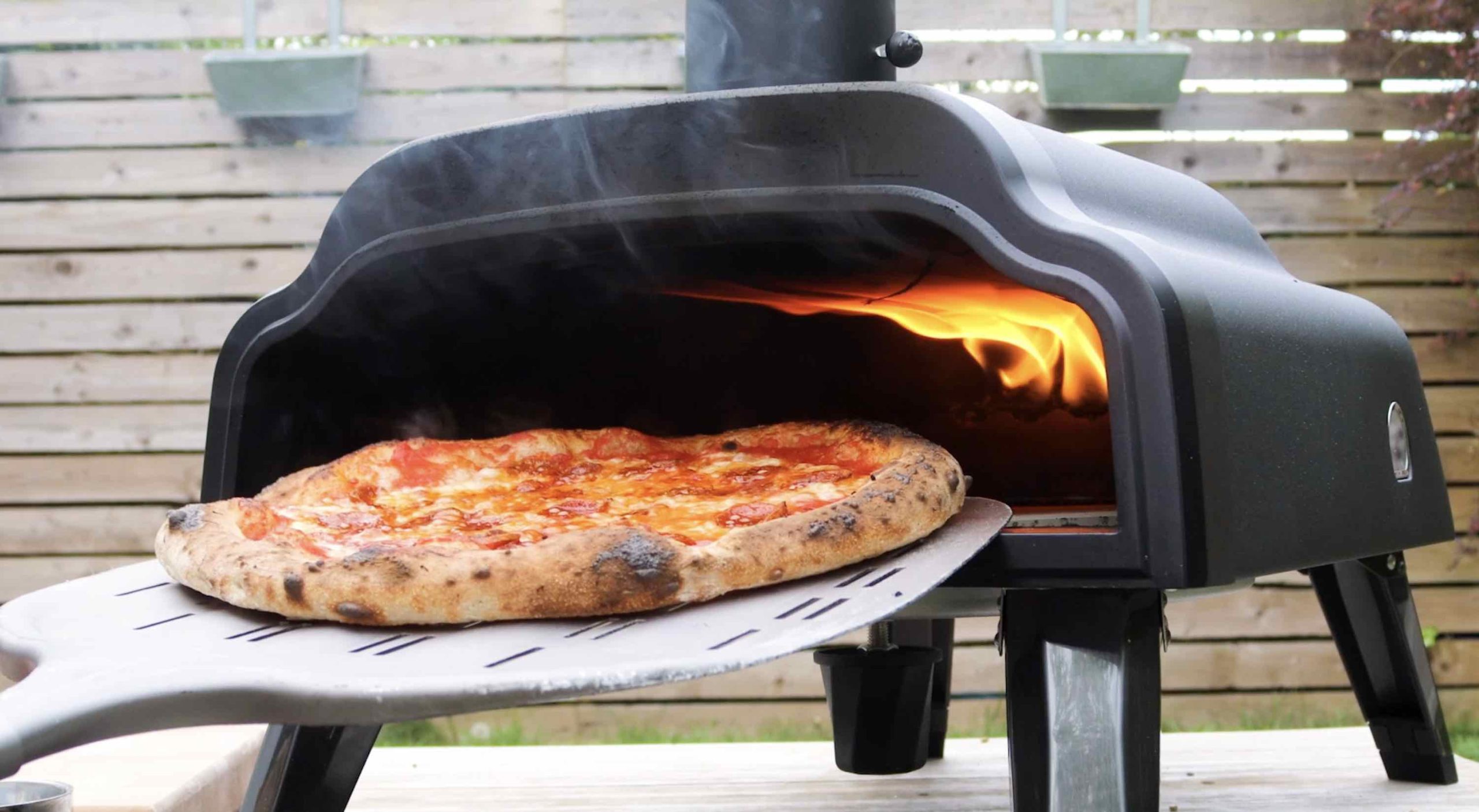 ręka wkładająca pizzę do rozgrzanego pieca opalanego drewnem